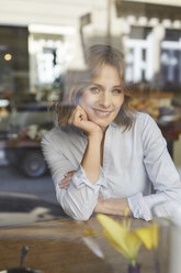 Portrait of smiling woman in a coffee shop looking out of window - PNEF00799