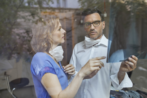 Porträt eines Radiologen und einer Krankenschwester hinter einer Fensterscheibe, die ein Röntgenbild betrachten, lizenzfreies Stockfoto