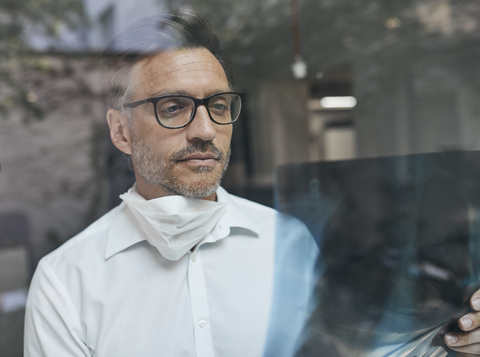 Porträt eines Radiologen hinter einer Fensterscheibe, der ein Röntgenbild betrachtet, lizenzfreies Stockfoto