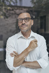 Portrait of man with stubble behind windowpane wearing white shirt and glasses - PNEF00821