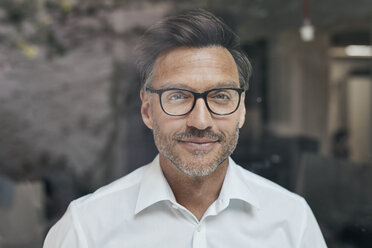Portrait of man with stubble behind windowpane wearing white shirt and glasses - PNEF00824