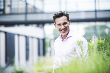 Portrait of smiling businessman outside office building - UUF14661