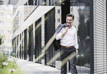 Smiling businessman walking outside office building - UUF14680