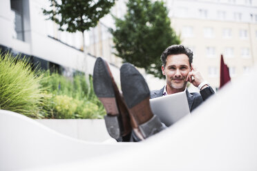 Porträt eines entspannten Geschäftsmannes mit Laptop vor einem Bürogebäude - UUF14692