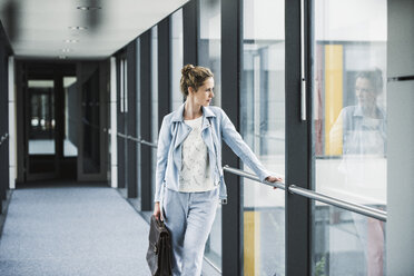 Businesswoman looking out of window in office passageway - UUF14696