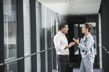 Businesswoman and businessman discussing in office passageway - UUF14702