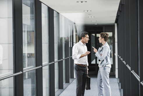 Businesswoman and businessman discussing in office passageway - UUF14704