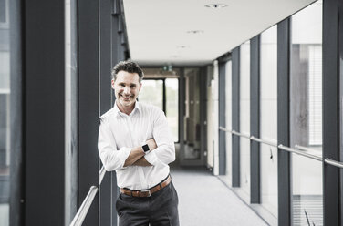 Portrait of smiling businessman in office passageway - UUF14725