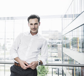 Portrait of confident businessman leaning on railing in office building - UUF14727