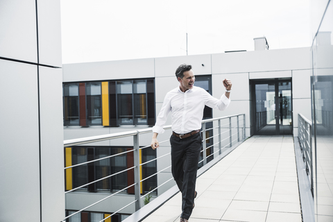 Jubelnder Geschäftsmann auf dem Skywalk eines Bürogebäudes, lizenzfreies Stockfoto