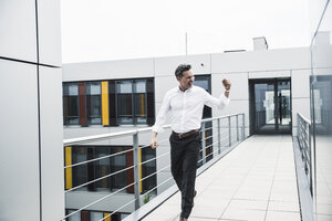 Jubelnder Geschäftsmann auf dem Skywalk eines Bürogebäudes - UUF14728