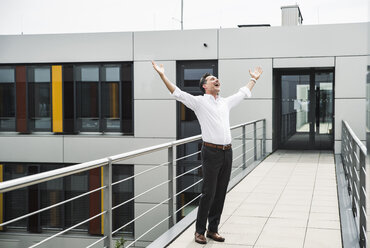 Cheering businessman standing on skywalk at office building - UUF14729