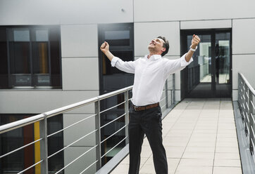 Cheering businessman standing on skywalk at office building - UUF14730