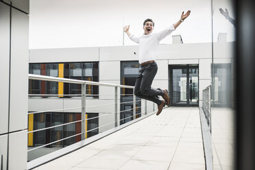 Cheering businessman jumping on skywalk at office building - UUF14731