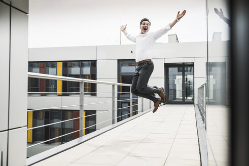 Ein jubelnder Geschäftsmann springt auf dem Skywalk eines Bürogebäudes - UUF14731