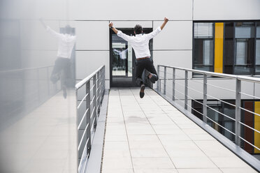 Cheering businessman jumping on skywalk at office building - UUF14732