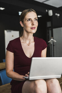 Geschäftsfrau im Büro in burgunderrotem Kleid mit Laptop - UUF14739