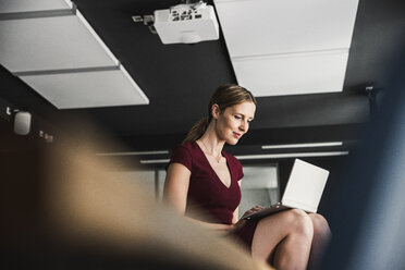 Geschäftsfrau im Büro in burgunderrotem Kleid mit Laptop - UUF14744