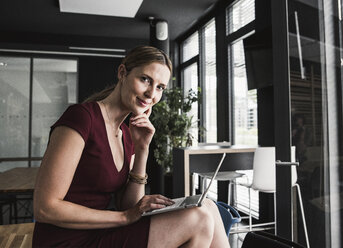 Geschäftsfrau im Büro in burgunderrotem Kleid mit Laptop - UUF14745