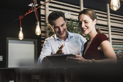 Lächelnde Geschäftsfrau und Geschäftsmann mit Tablet diskutieren im Büro - UUF14759