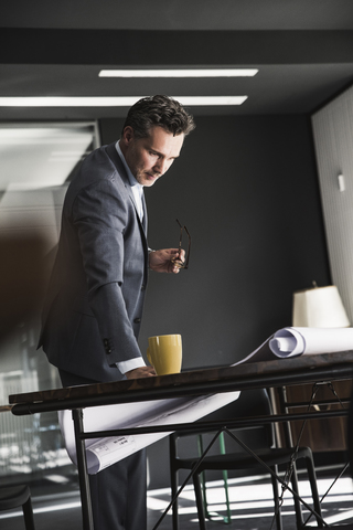 Geschäftsmann im Büro betrachtet einen Plan auf dem Schreibtisch, lizenzfreies Stockfoto