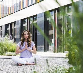 Frau übt Yoga im Garten vor einem Bürogebäude - UUF14786