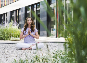 Frau übt Yoga im Garten vor einem Bürogebäude - UUF14787