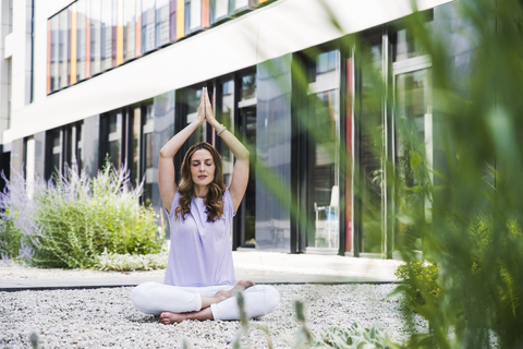 Frau übt Yoga im Garten vor einem Bürogebäude, lizenzfreies Stockfoto
