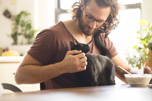 Young man stroking his black cat at home - MFRF01155