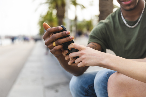 Die Hände eines multikulturellen jungen Paares halten ein Smartphone, Nahaufnahme, lizenzfreies Stockfoto