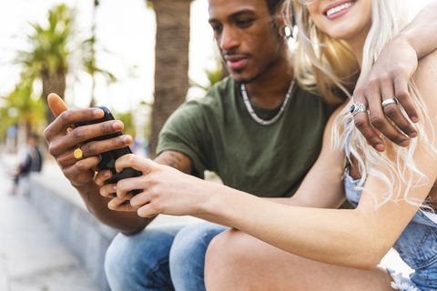 Ein junges multikulturelles Paar hält ein Smartphone in den Händen, lizenzfreies Stockfoto