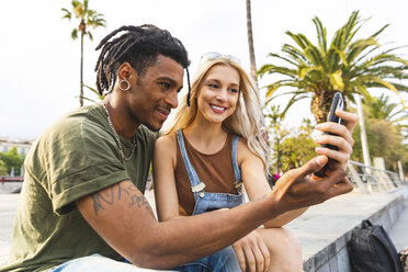 Lächelndes multikulturelles junges Paar schaut auf sein Smartphone - WPEF00714