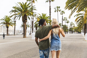 Spanien, Barcelona, Rückenansicht eines multikulturellen jungen Paares, das Arm in Arm auf der Promenade spazieren geht - WPEF00723