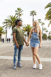 Spanien, Barcelona, multikulturelles junges Paar, das Hand in Hand auf der Promenade steht - WPEF00724