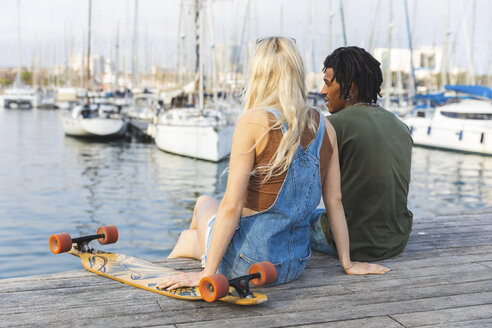 Spanien, Barcelona, multikulturelles junges Paar mit Longboard, das am Hafen entspannt - WPEF00733