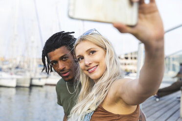 Porträt eines jungen multikulturellen Paares, das am Hafen ein Selfie mit seinem Smartphone macht - WPEF00734