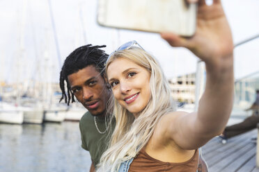 Portrait of multicultural young couple taking selfie with smartphone at harbour - WPEF00734