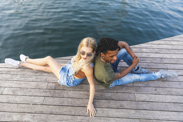 Multicultural young couple relaxing back to back on jetty - WPEF00737