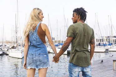 Back view of multicultural young couple standing hand in hand on jetty - WPEF00741