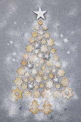 Star-shaped biscuits and Christmas baubles forming Christmas Tree on grey background - GWF05616