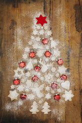 Christmas cookies and red star-shaped Christmas baubles forming Christmas Tree on wooden background - GWF05619