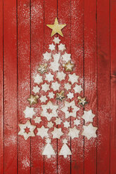 Christmas cookies and star-shaped Christmas baubles forming Christmas tree on red wooden background - GWF05621