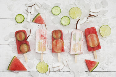 Homemade watermelon and coconut cream ice lollies with lime and cucumber slices, fresh coconut chips on ice cubes - GWF05624