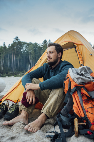 Rucksacktourist sitzt vor seinem Zelt am Strand, lizenzfreies Stockfoto