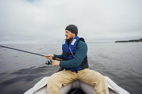 Mann sitzt auf einem Boot und fischt mit einer Angelrute - VPIF00427