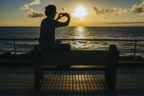 Spanien, Kanarische Inseln, Gran Canaria, Mann fotografiert mit Mobiltelefon bei Sonnenuntergang - KIJF01976