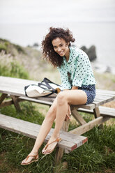 Young woman sitting on picnic table smiling, portrait - ISF19170