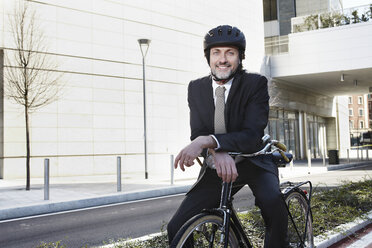 Mid adult businessman sitting on bike, smiling - ISF19272