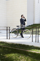 Mid adult businessman holding bicycle and using mobile phone - ISF19273