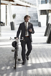 Mittlerer erwachsener Geschäftsmann, der mit dem Fahrrad spazieren geht und ein Mobiltelefon benutzt - ISF19275